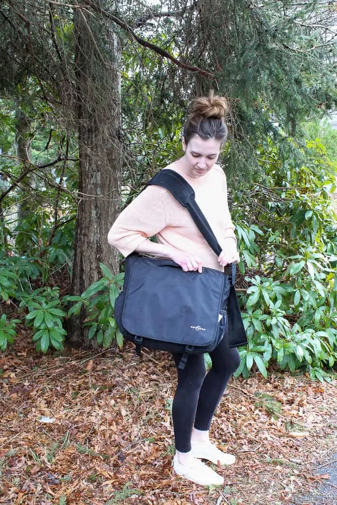 Woman models convertible bag next to wooded area.