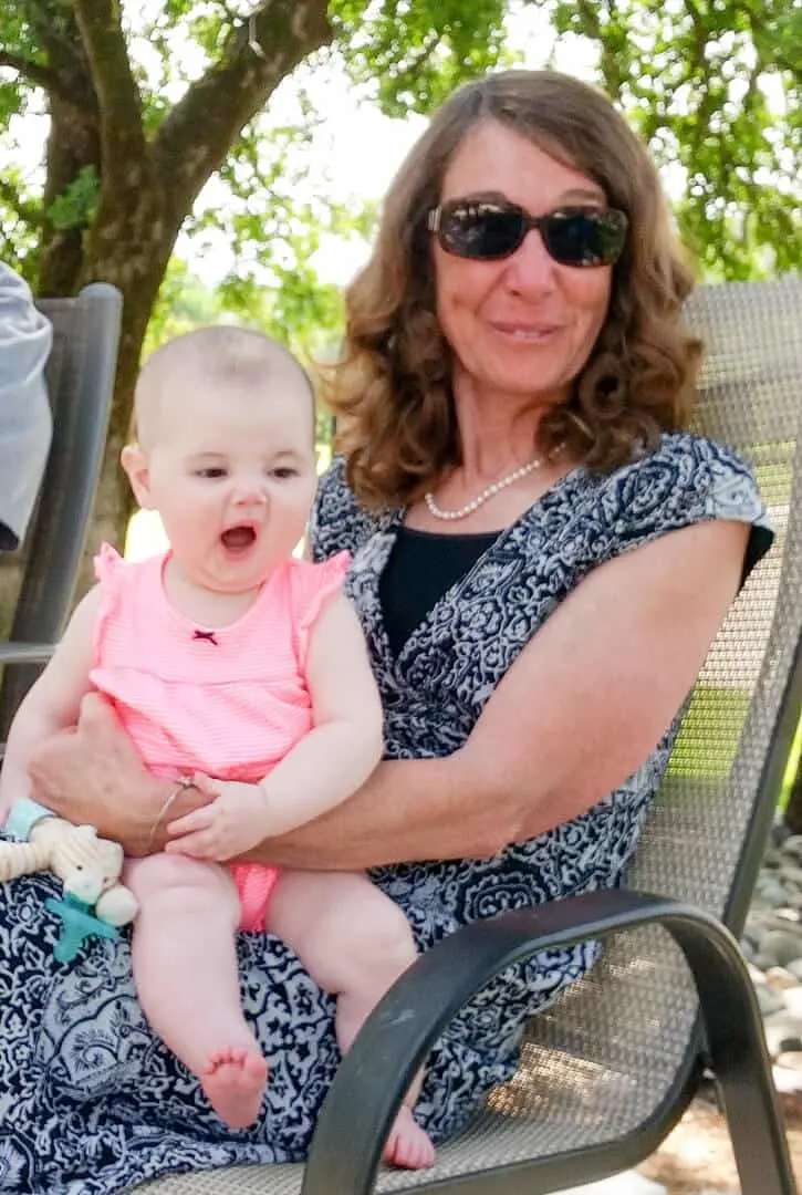 Woman holds baby girl on patio furniture.