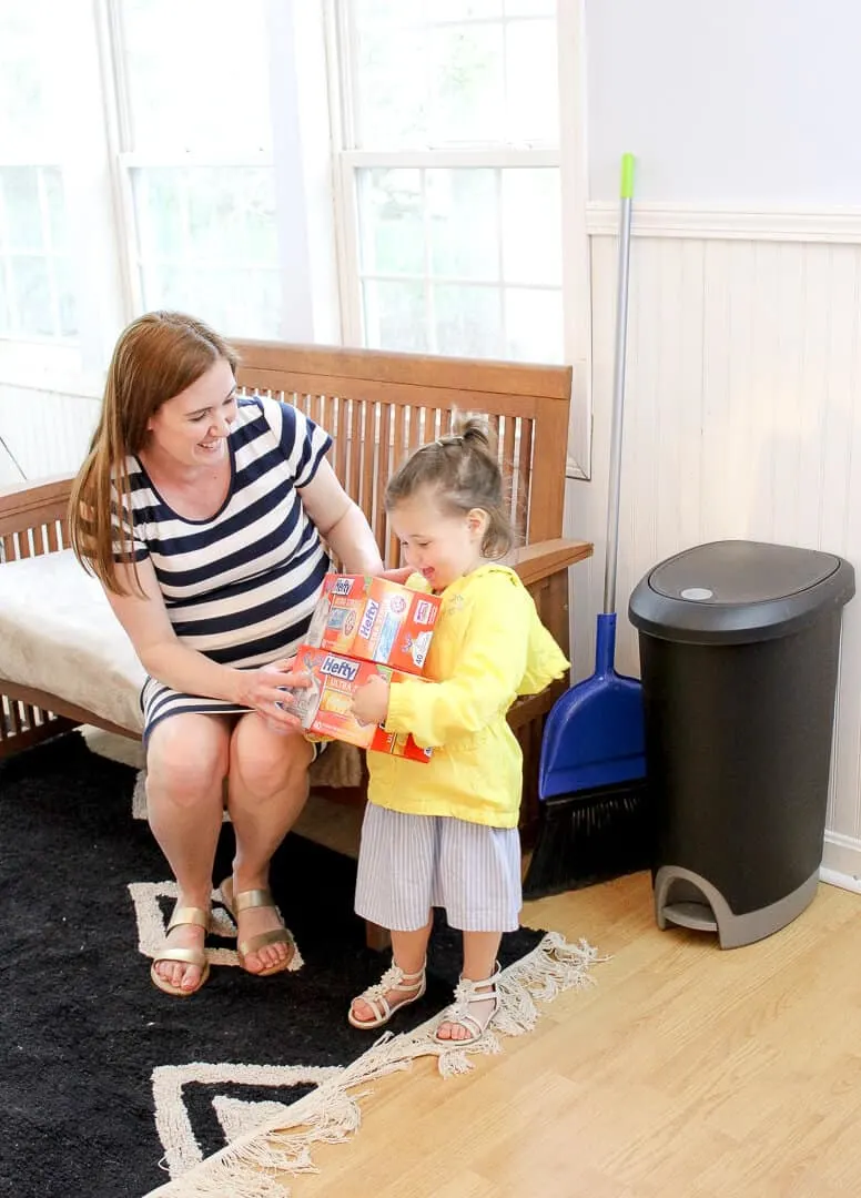 Toddler girl carries boxes of trash bags.