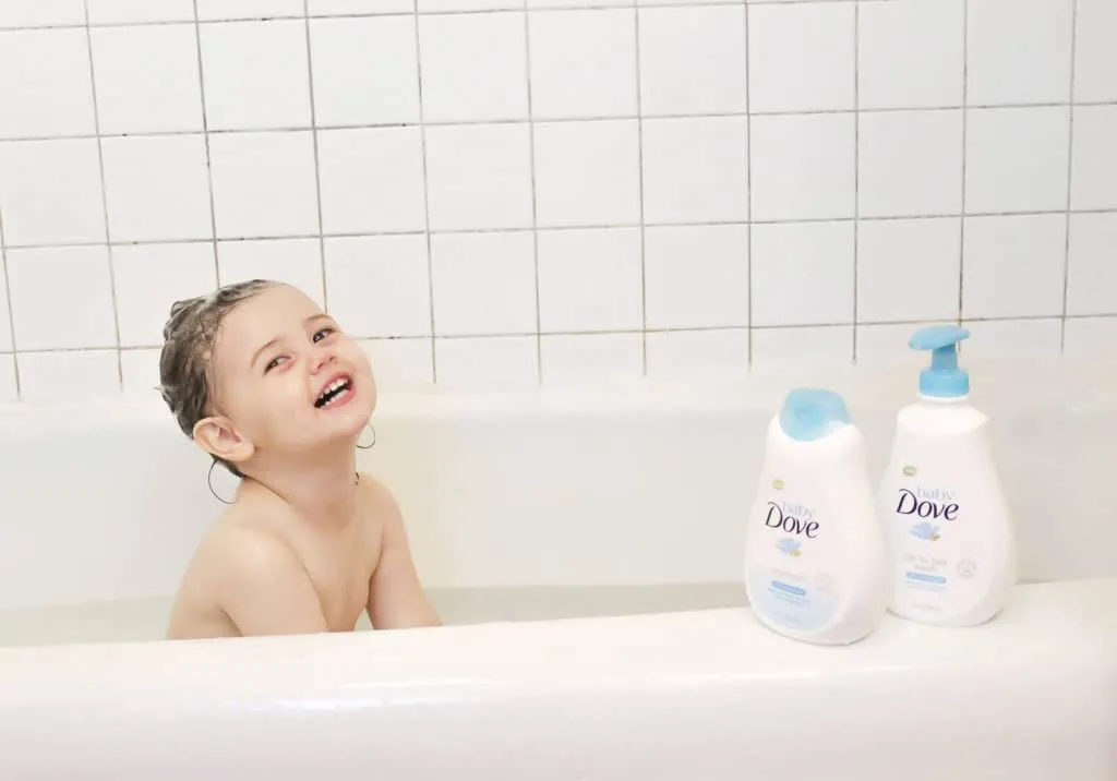 Little girl sits in bath next to Baby Dove products.
