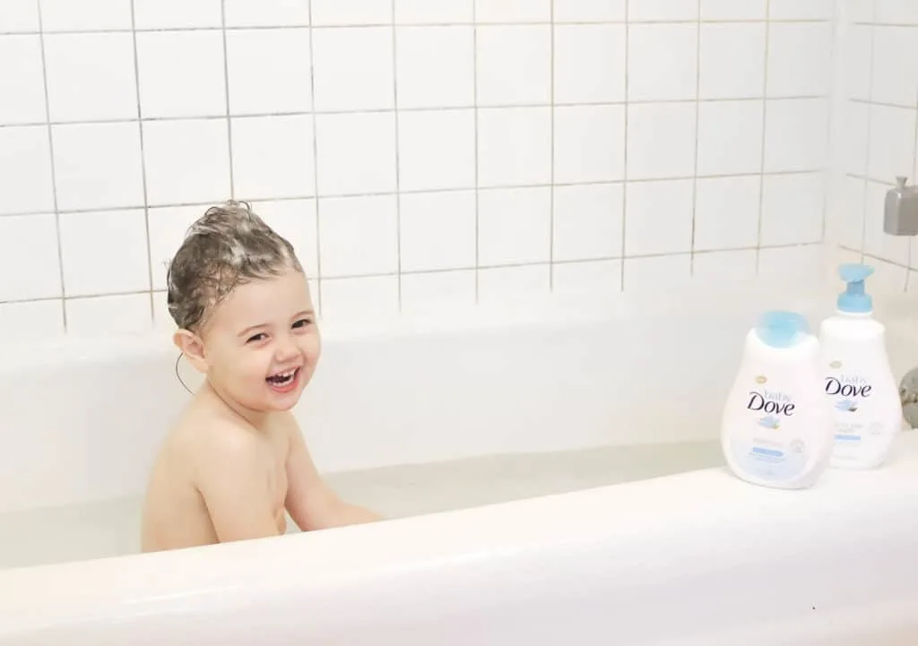 Baby Dove skin care products sit on side of tub with toddler in bath.