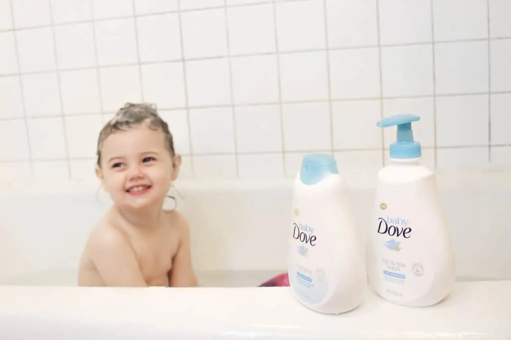 Toddler girl sits in tub with soapy hair.