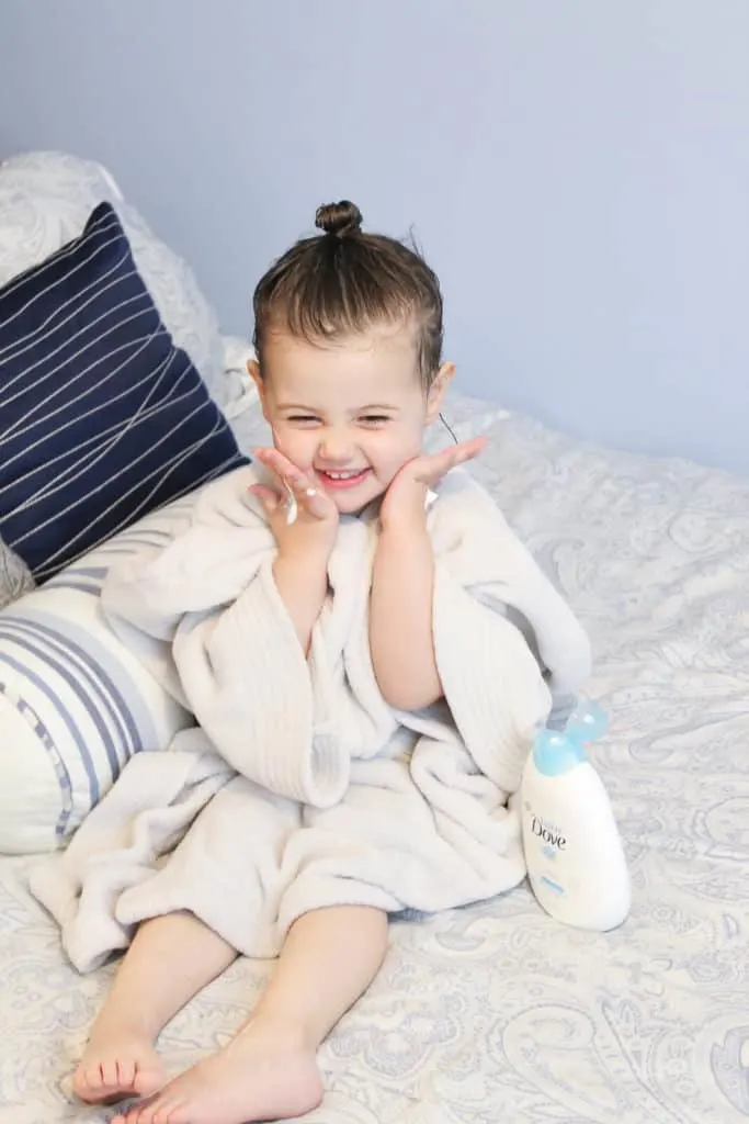 Toddler girl in bathrobe sits on bed.