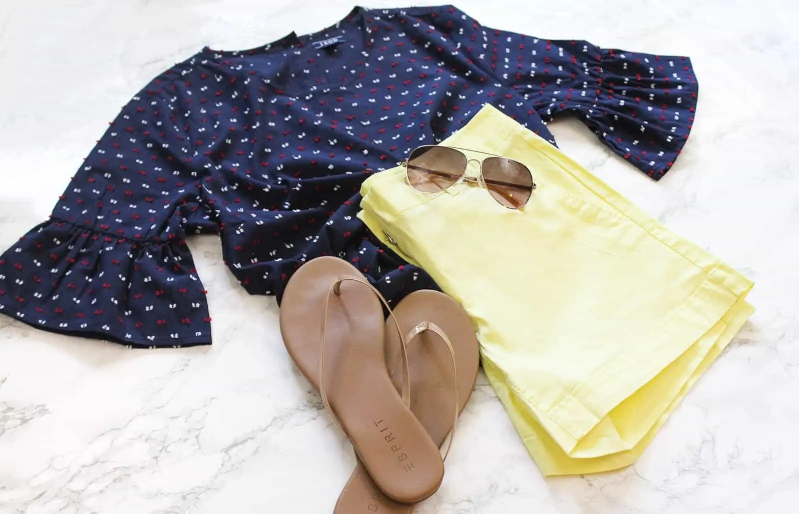 Summer outfit lays next to flip flops and sunglasses.