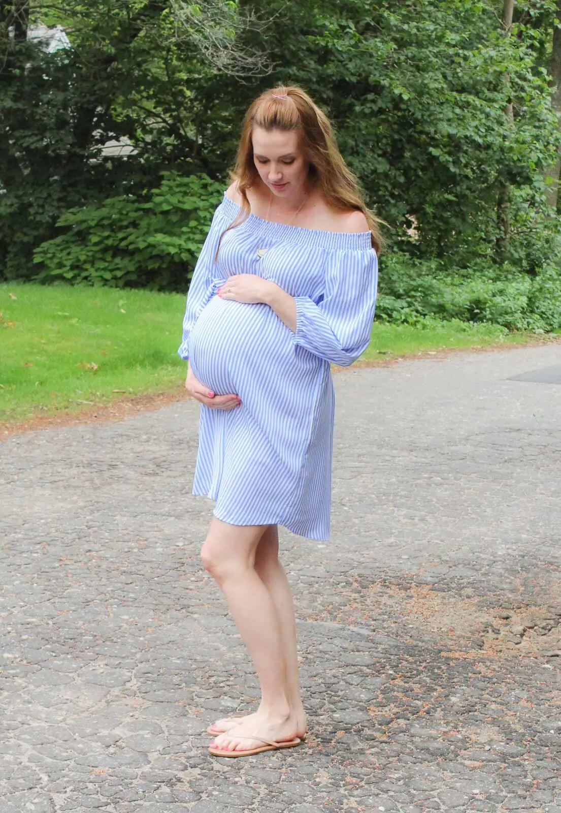 Pregnant woman cradles belly in off the shoulder summer dress.