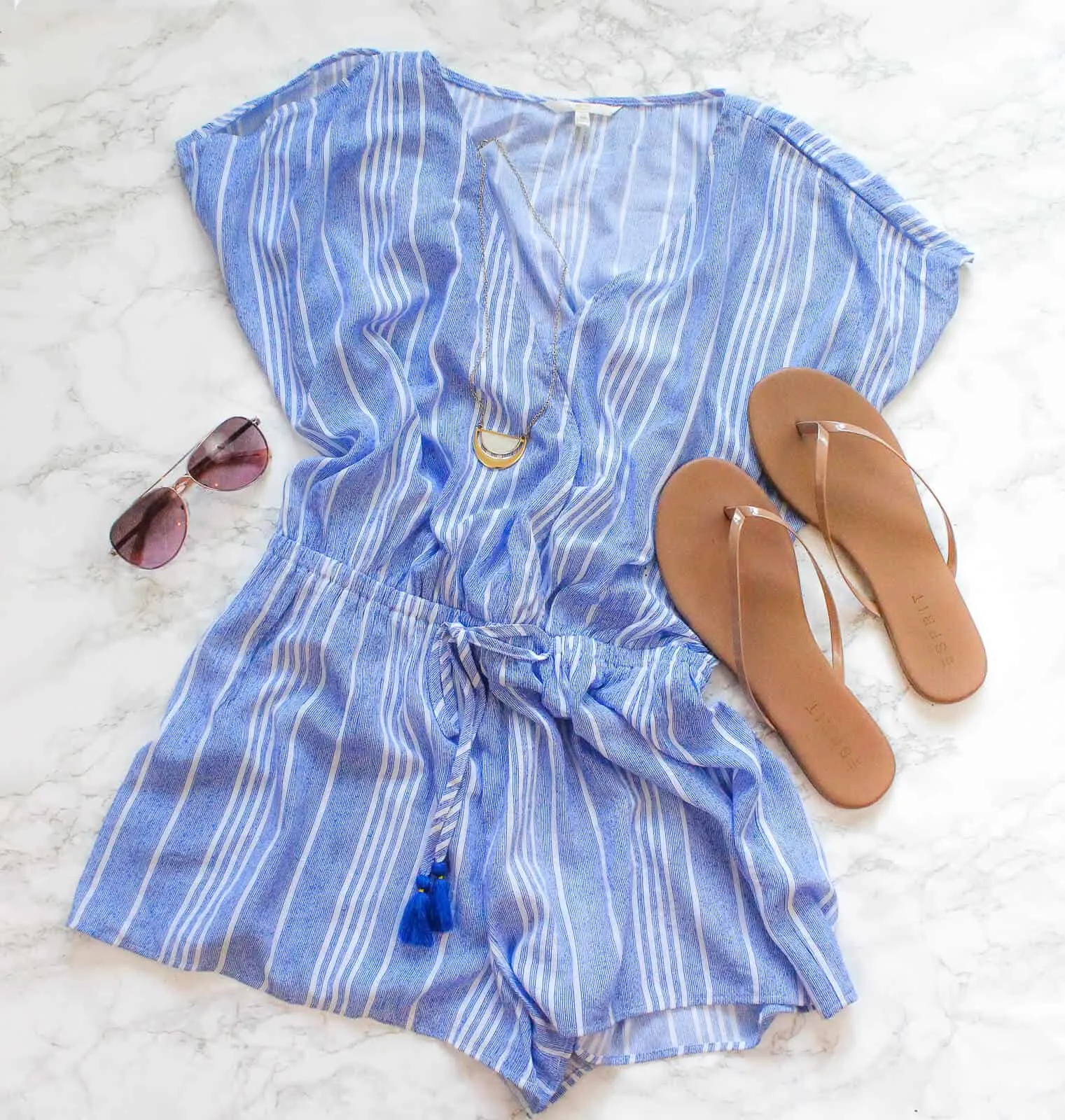 Blue summer dress next to flip flops and sunglasses.