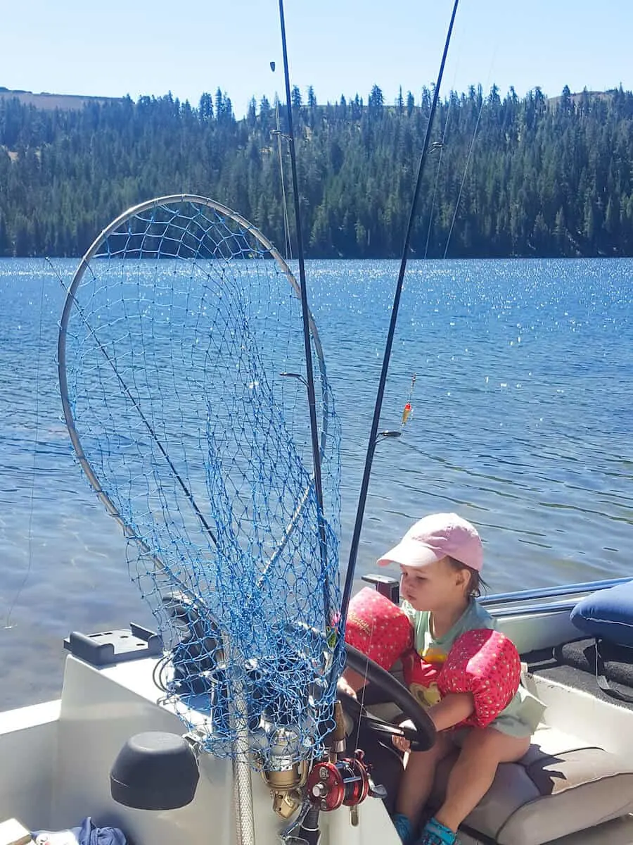 Toddler girl sits behind steering wheel of fishing boat.