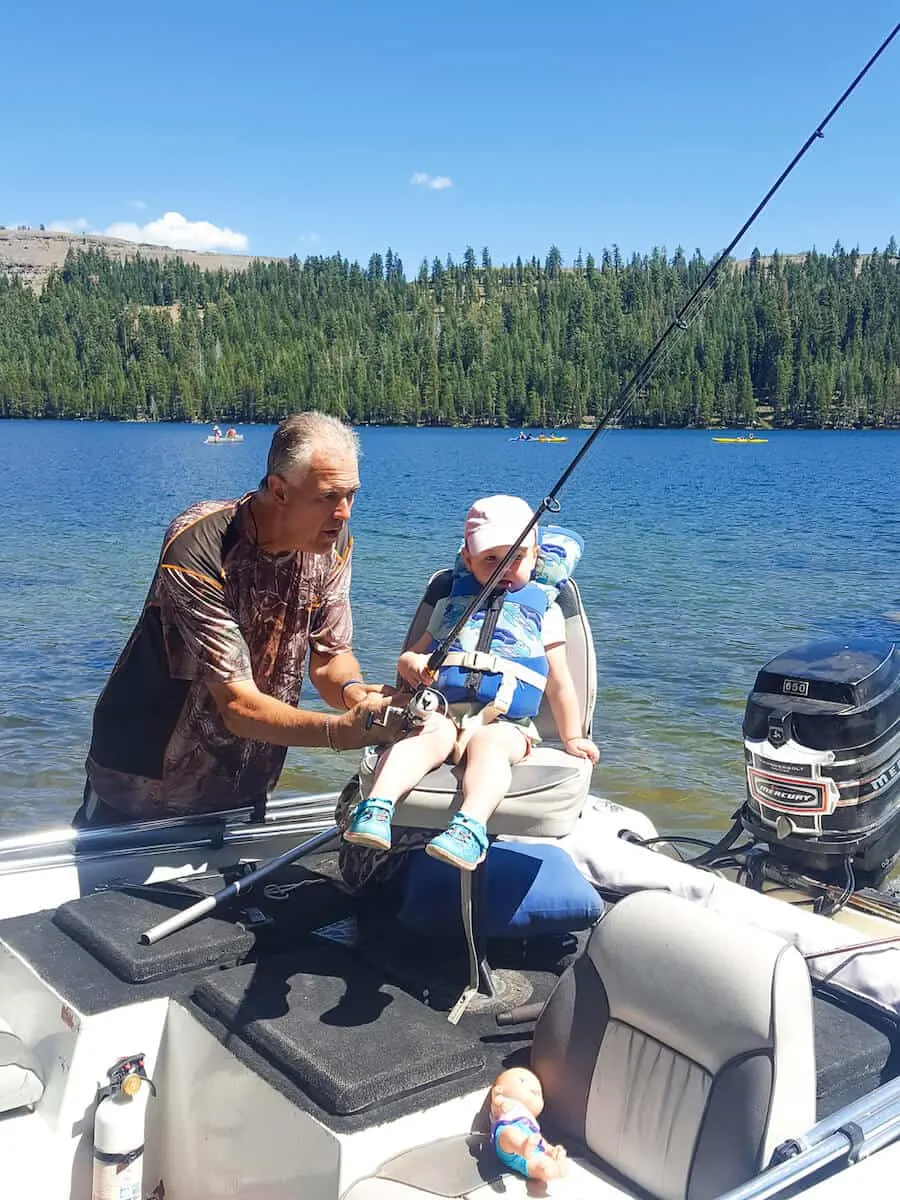 Man helps toddler girl hold fishing pole in boat.