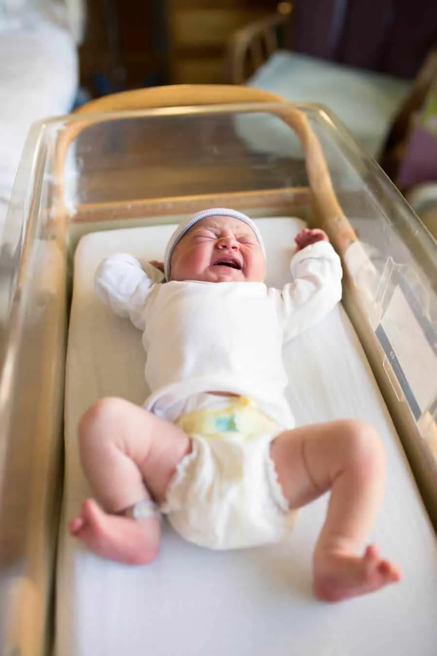 Newborn baby cries in hospital bed.