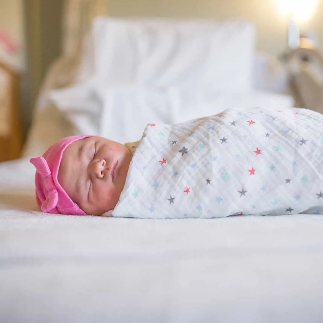 Swaddled newborn girl sleeps on hospital bed.