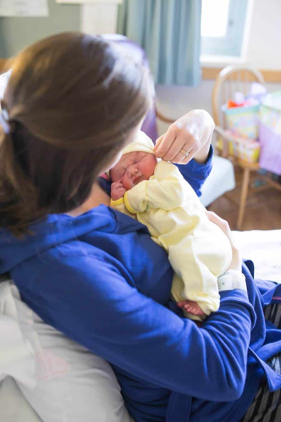 First time mom holds newborn wearing yellow outfit.