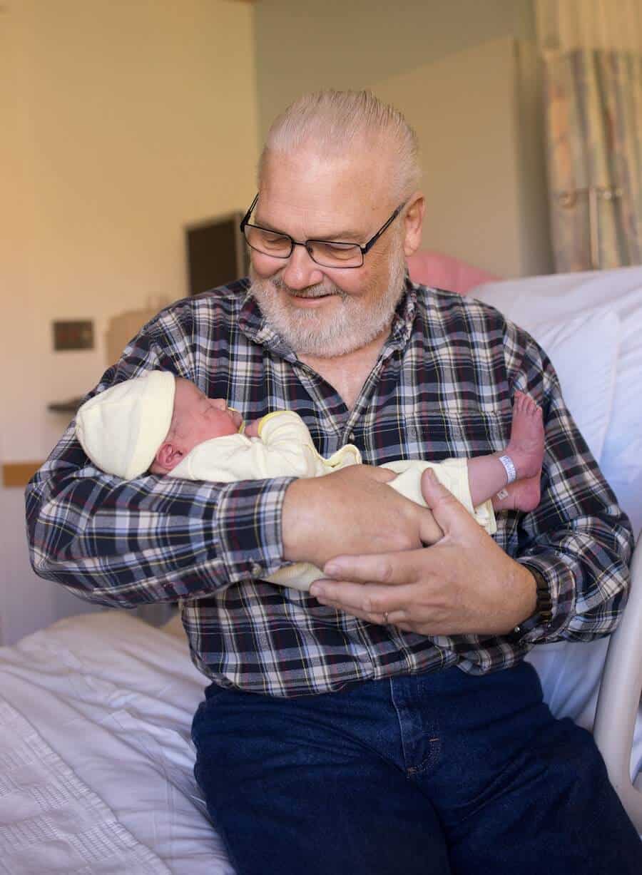 Grandfather holds newborn granddaughter in hospital.