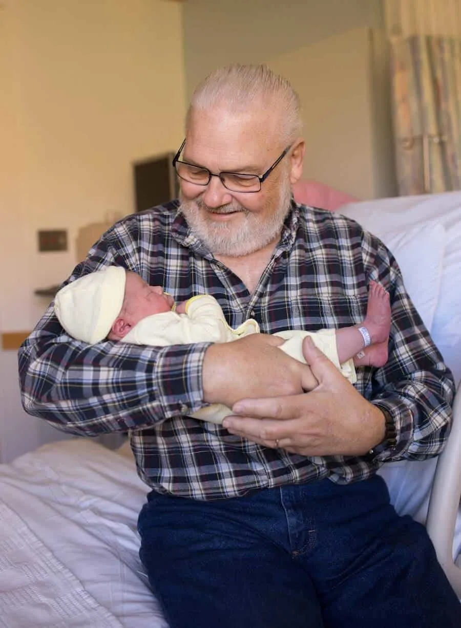 Grandfather holds newborn granddaughter in hospital.