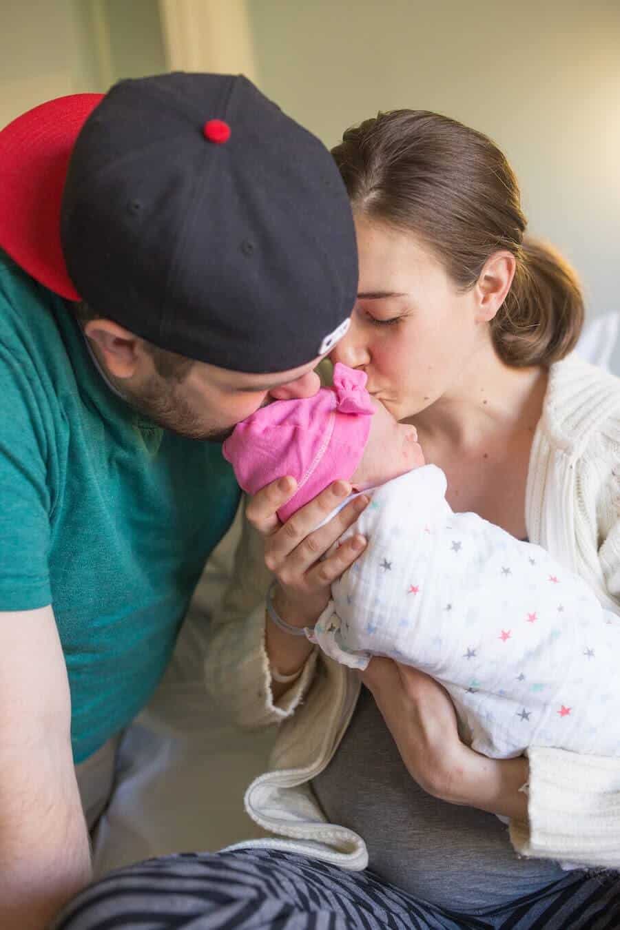 Couple holds and kisses newborn baby girl.