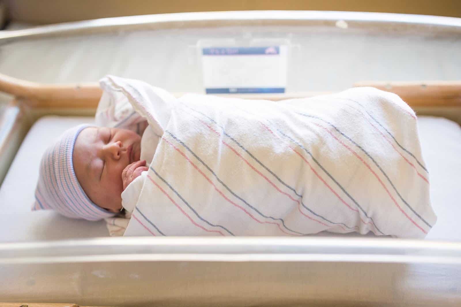 Newborn sleeps in hospital blanket swaddle.