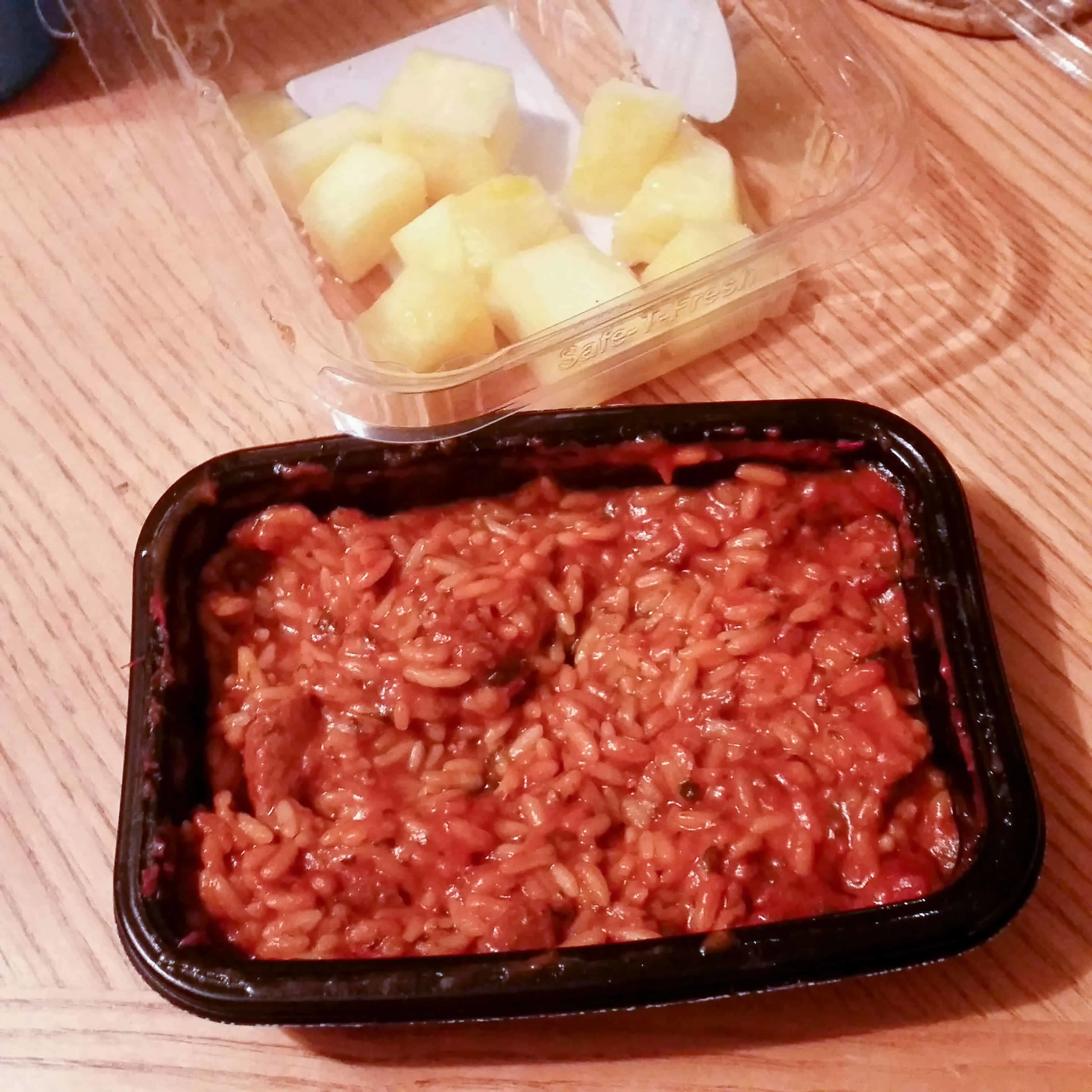 Spicy food next to container of pineapple chunks.