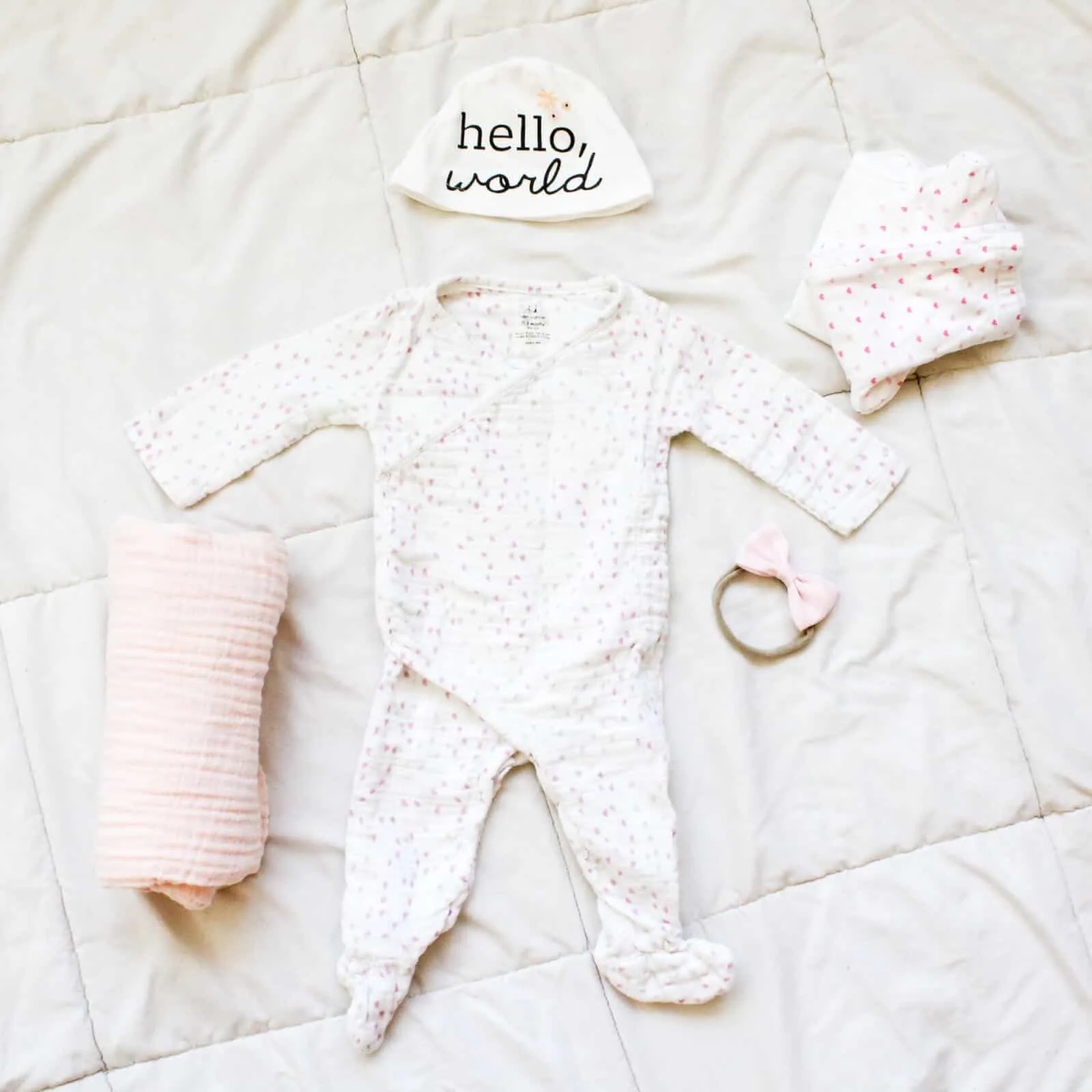 Newborn baby outfit and blanket on bed.