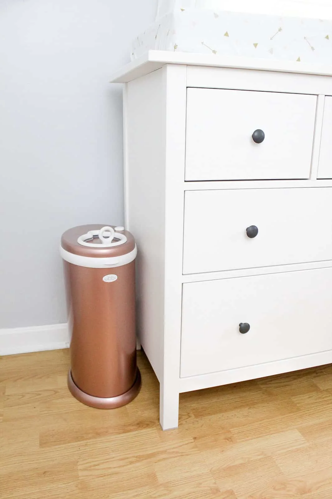 Golden diaper pail next to white dresser.