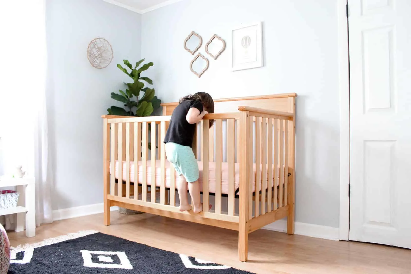 Toddler girl climbs into crib in nursery room.