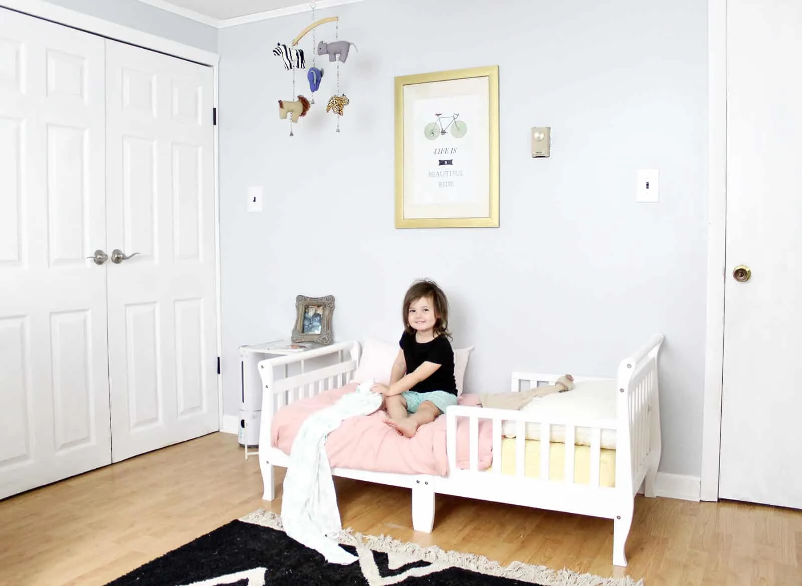 Toddler girl sits on white toddler bed in nursery.