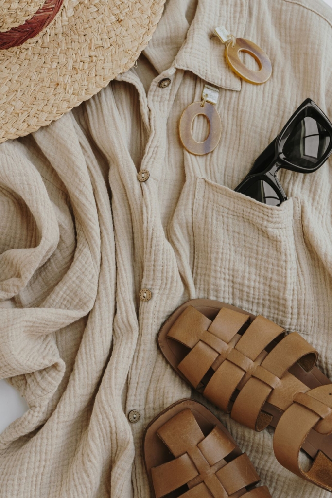 Flat lay outfit with a flowy cream top, straw hat, and sandals.