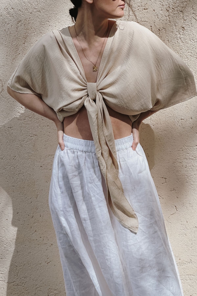 A woman in a cream cropped shirt and flowy white skirt.