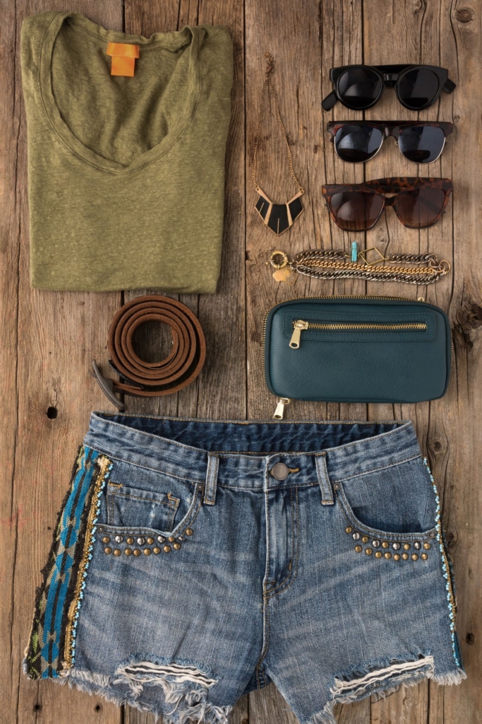 Flat lay outfit with with jean shorts, a green top, and teal bag.