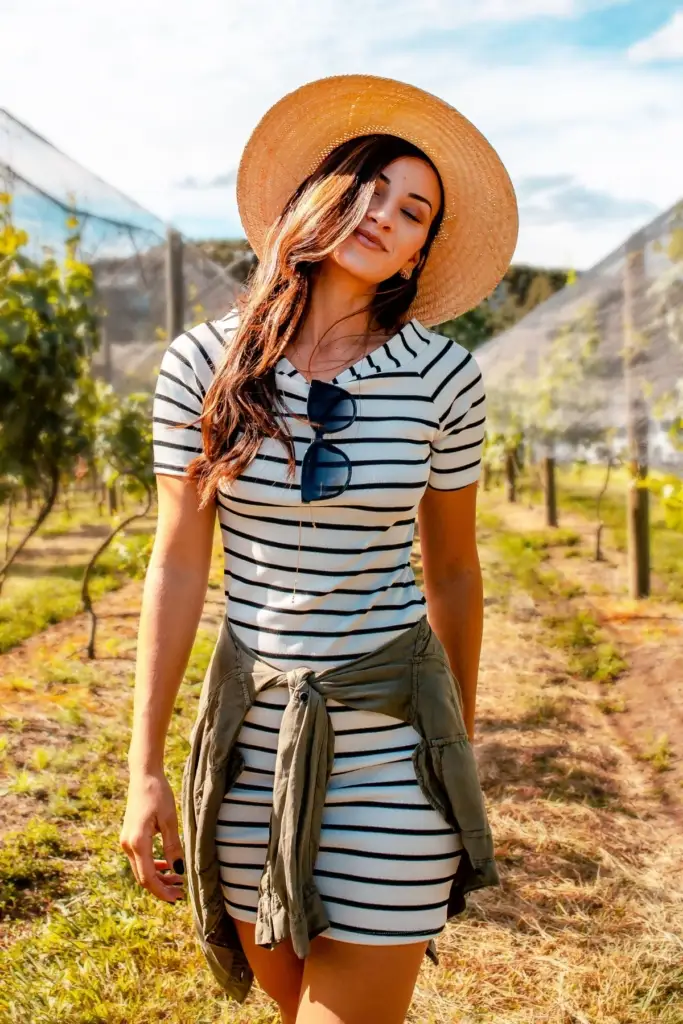 A woman in a black and white middy dress with a straw hat in a vineyard.