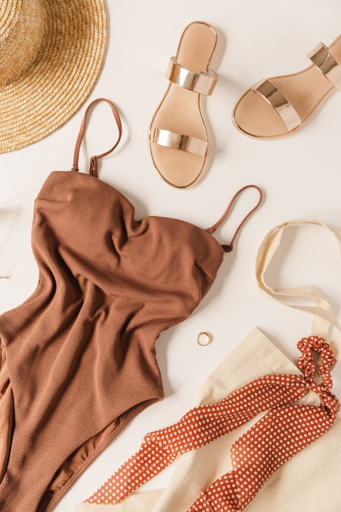 A brown one piece swimsuit with champagne sandals.
