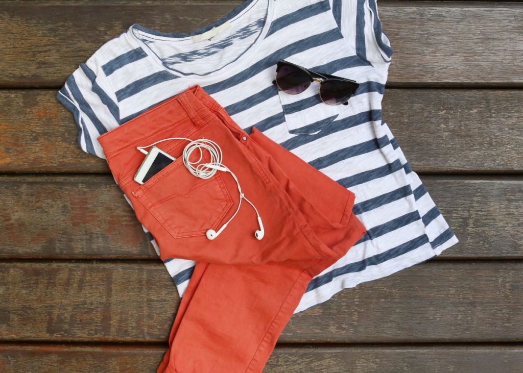 Flat lay outfit with with a blue and white striped shirt, coral pants, and sunglasses.