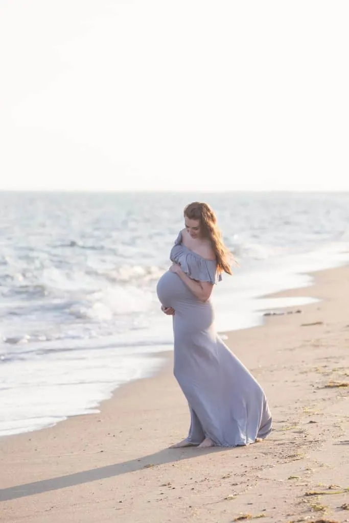 Woman wears flowy maternity dress for pictures on beach.