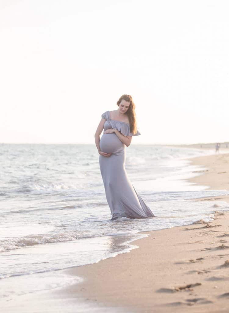 Woman walks on shoreline for maternity shoot on beach.
