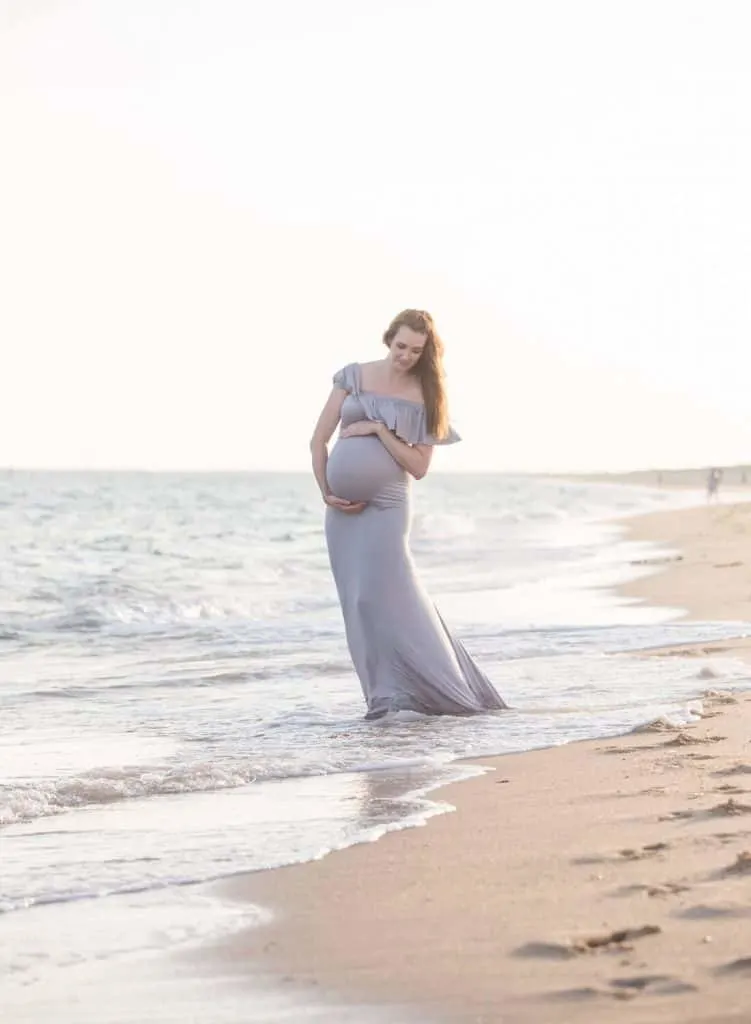 Woman walks on shoreline for maternity shoot on beach.