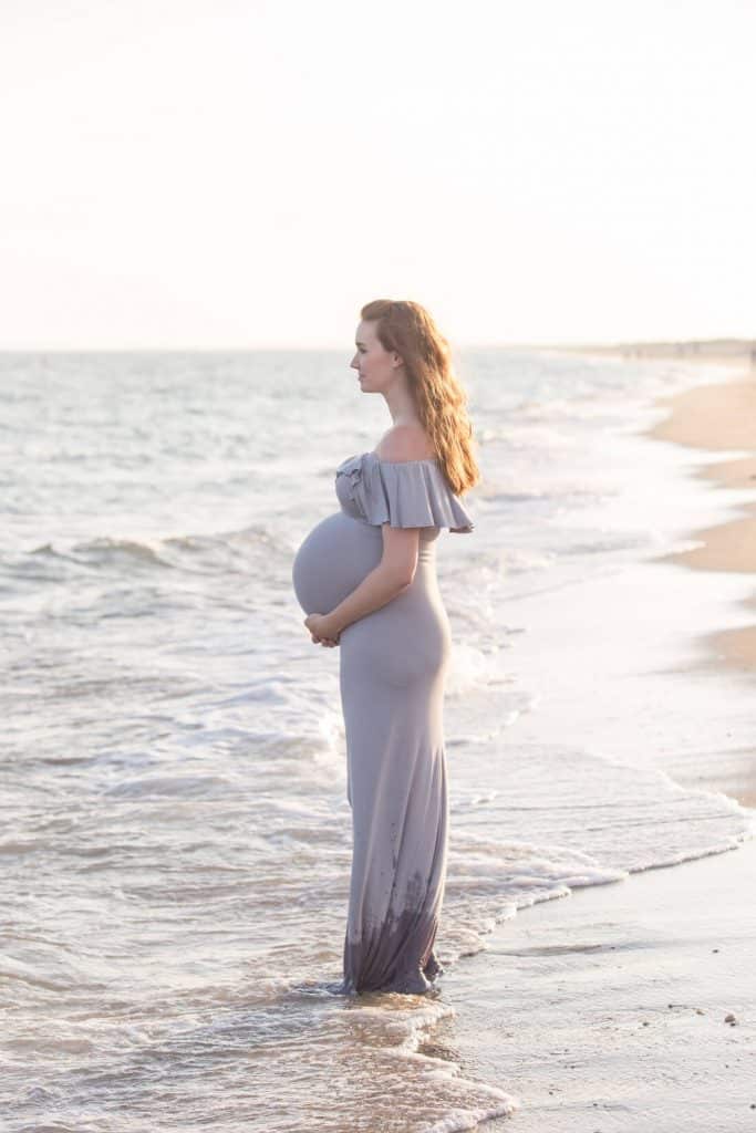 Woman stands at waters edge for pregnancy photos.
