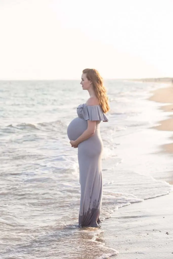 Woman stands at waters edge for pregnancy photos.