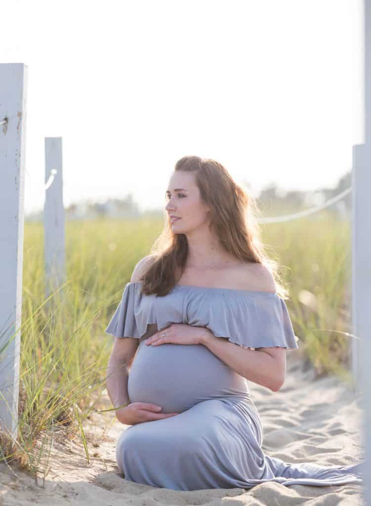Woman sits on sandy path for maternity photo shoot.