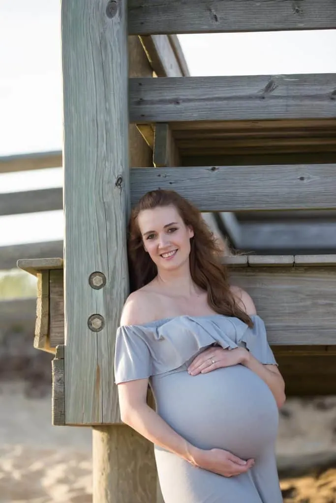 Woman takes maternity pictures in front of dock at beach.