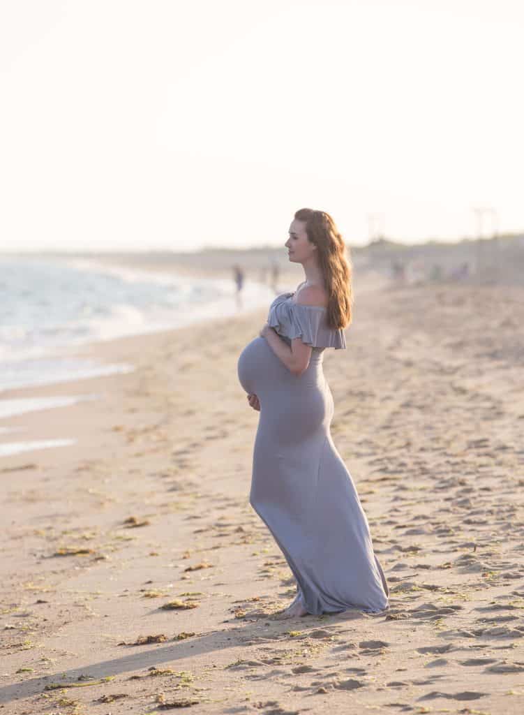 Woman poses for maternity photos on beach.