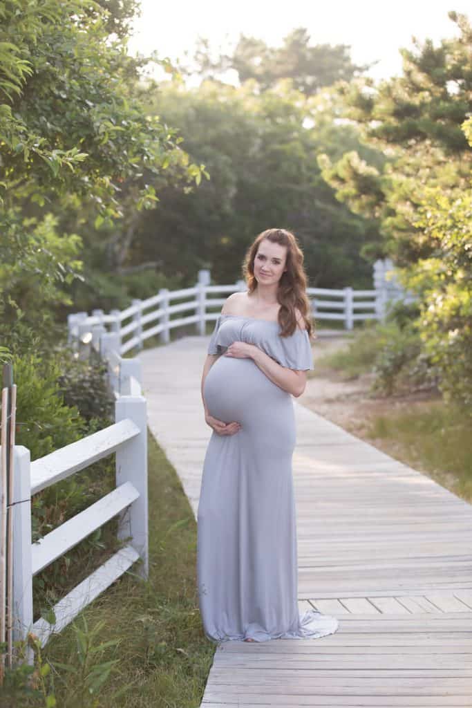 Woman poses in maxes dress for maternity pictures.