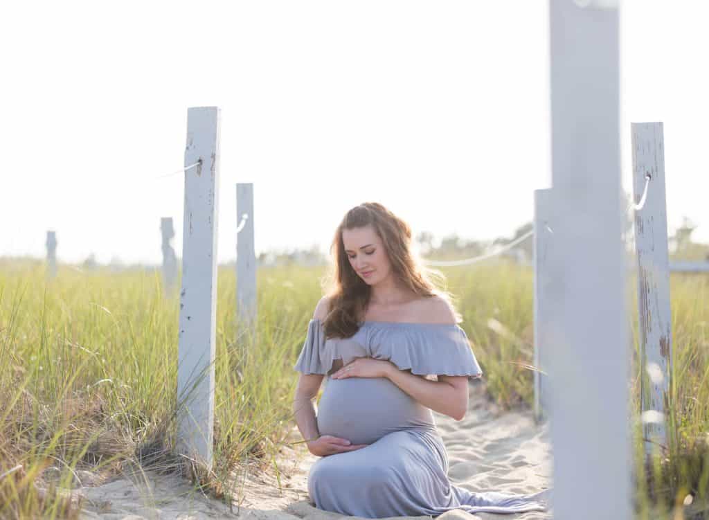 Woman sits on path to beach for maternity pictures.