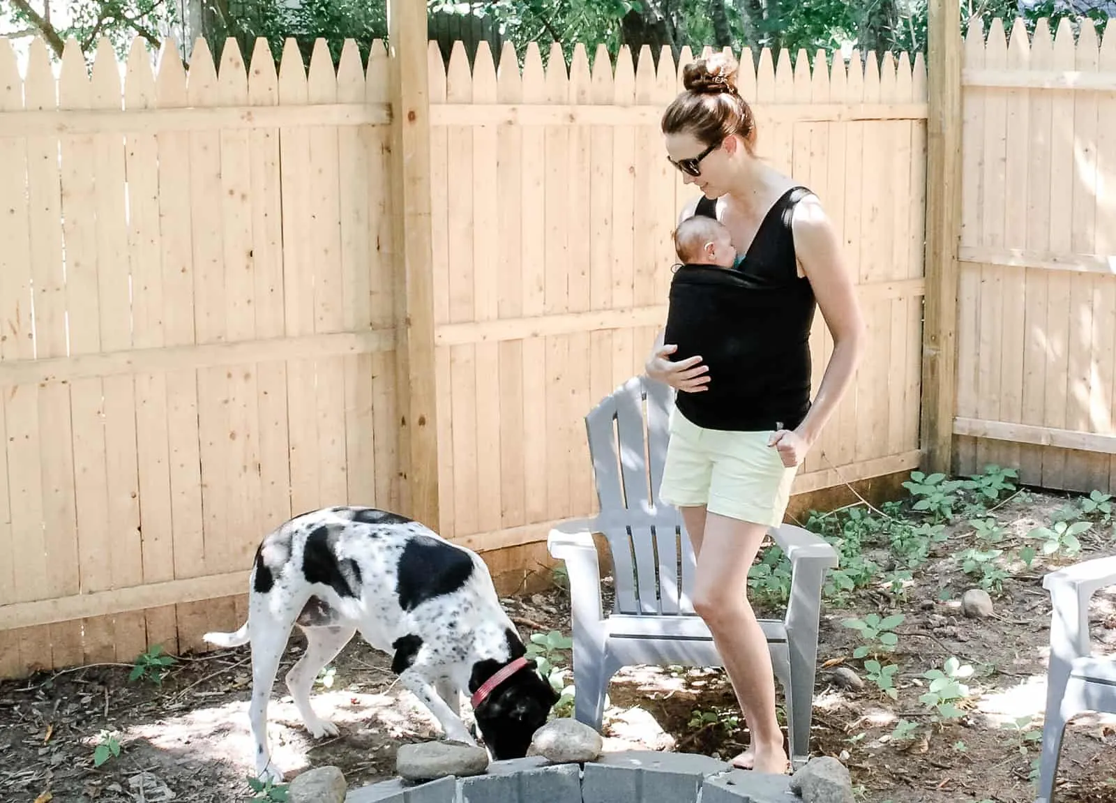 Woman wears baby in sling while outdoors with family dog.