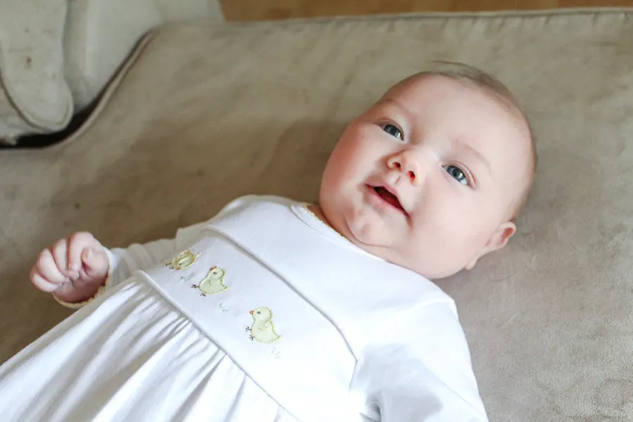 Baby wears white dress with yellow baby chicks.