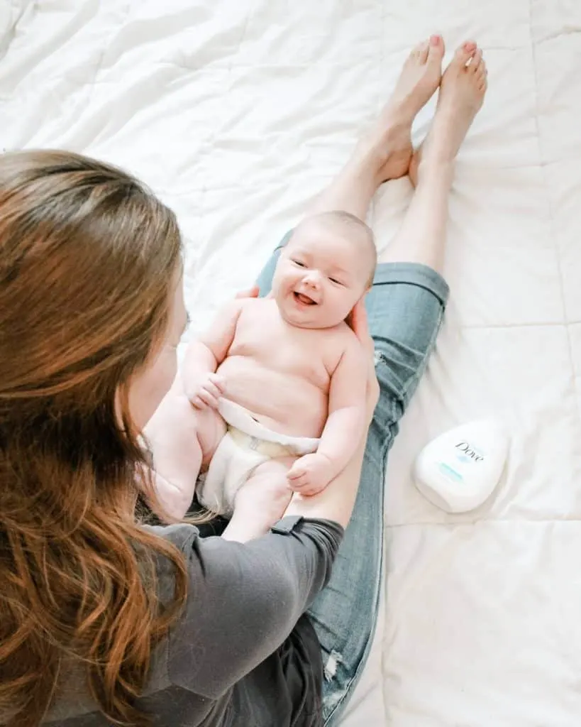 Baby holds baby over legs next to bottle of Baby Dove lotion.