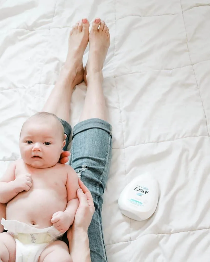 Mom holds baby on bed next to bottle of Baby Dove lotion.