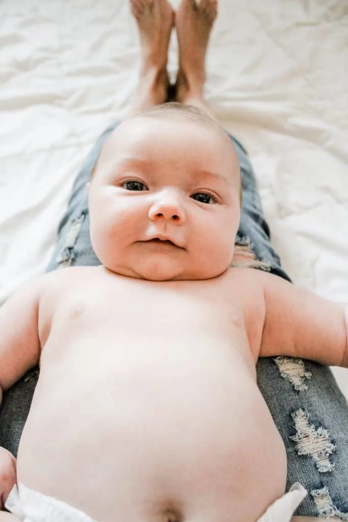 Baby lays over mothers legs and stares into the camera.