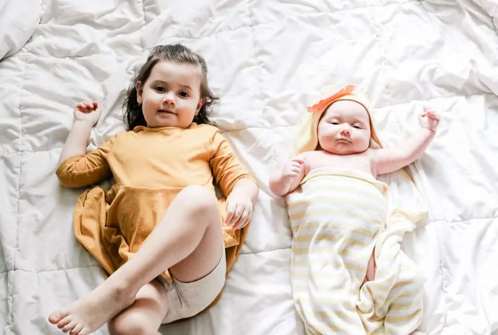 Little girl and baby lay on bed.