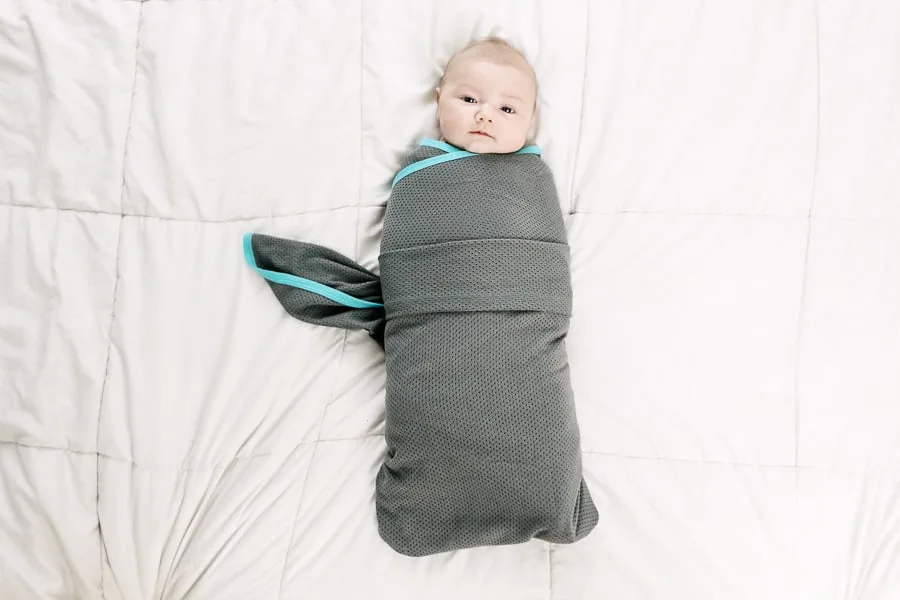 Baby lays on bed in swaddle for tutorial.
