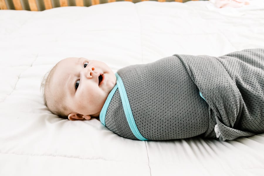 Baby wears grey and teal swaddle.