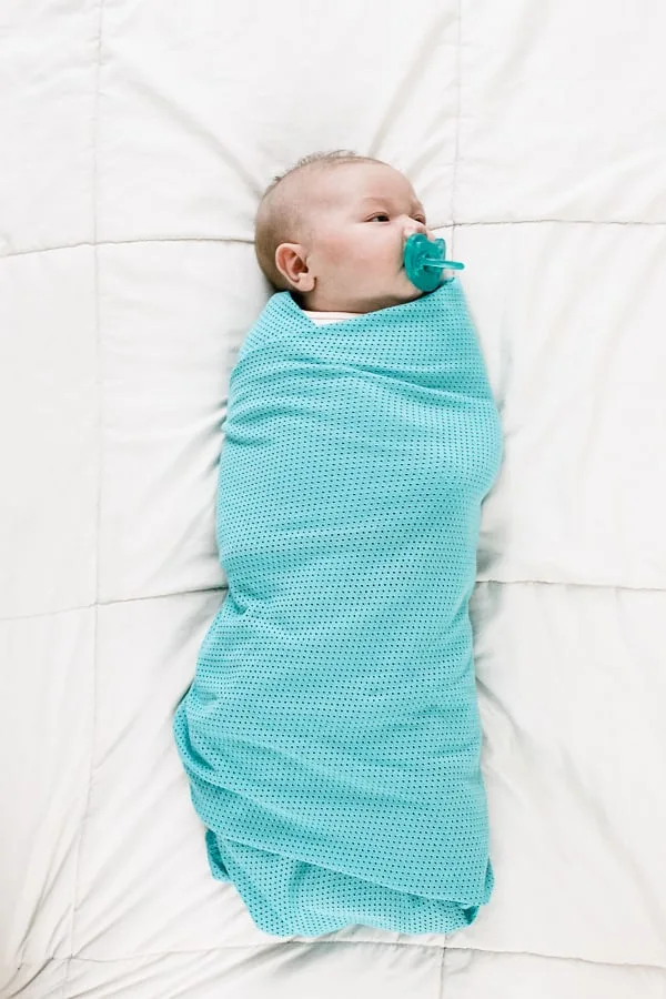 Baby wrapped in teal swaddle.
