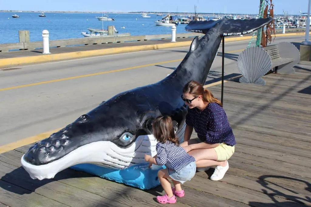 Woman and toddler girl play at whale statue.